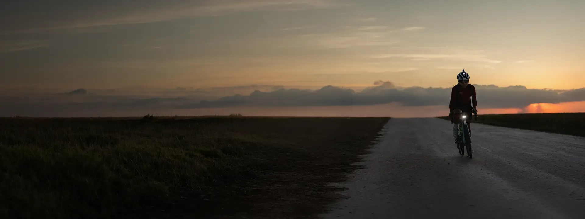 Cyclist riding towards the camera on a quiet road at sunset with a front light illuminated