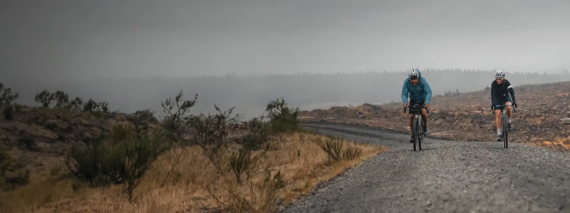 Two cyclists climbing a gravel track through open moorland in misty conditions