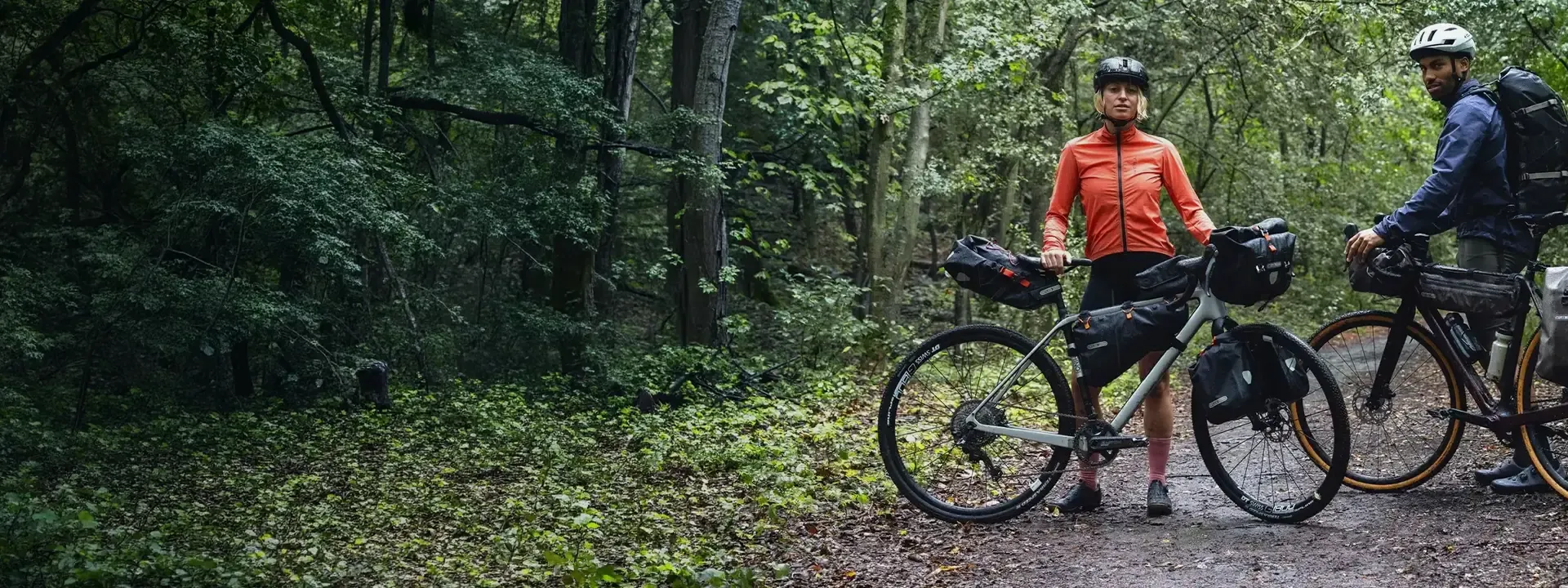 Two bikepackers with frame bags on loaded bikes in woodland