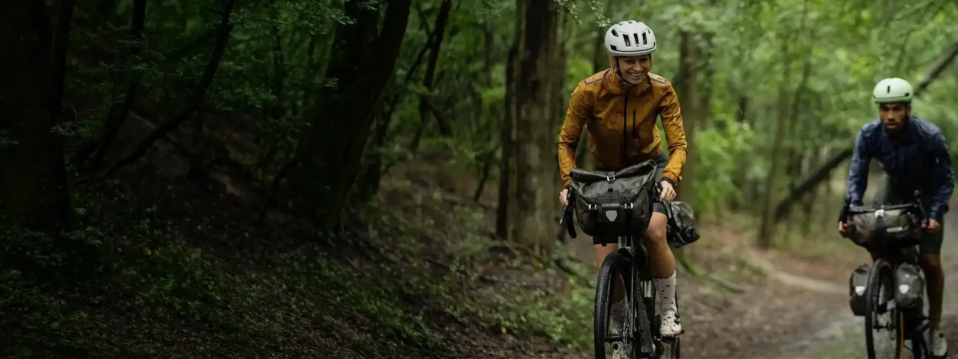 Two bikepackers riding with handlebar bags on a woodland trail