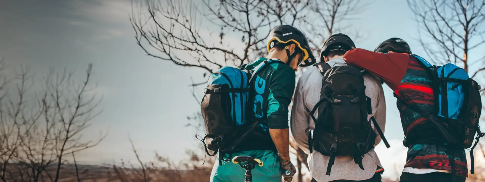 Three mountain bikers wearing trail backpacks beside their bikes