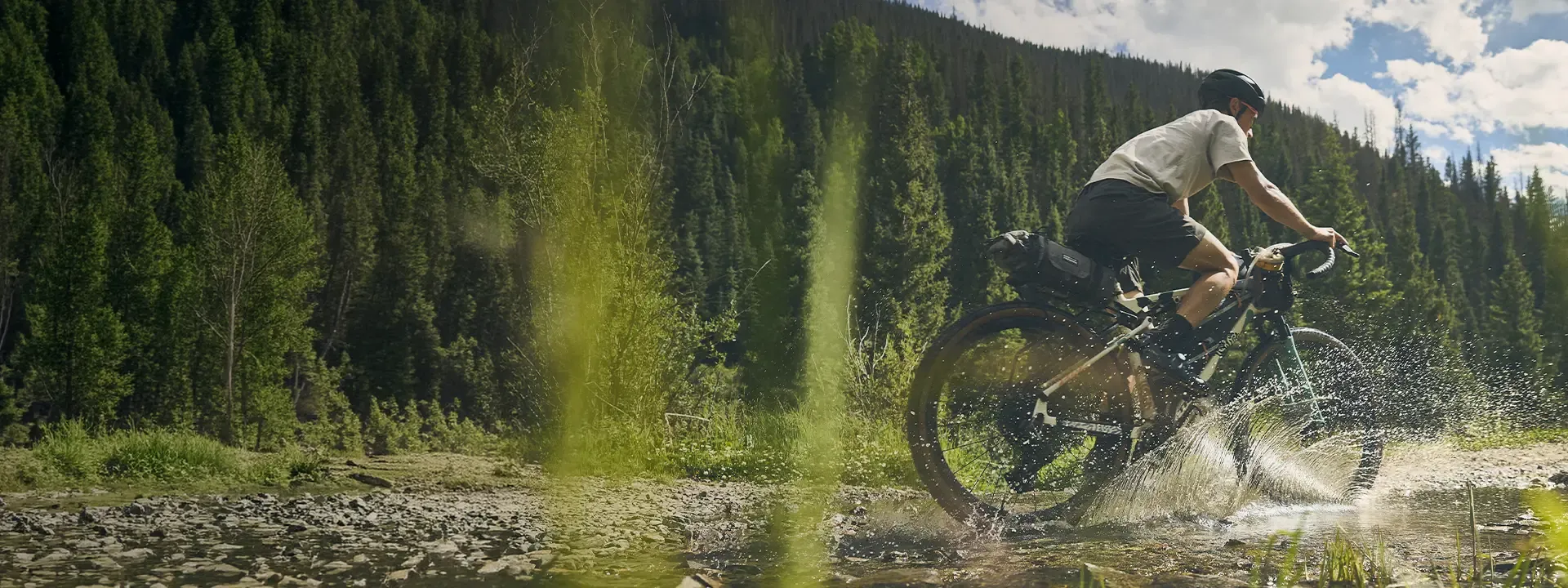 Cyclist crossing a shallow stream with a large saddle bag