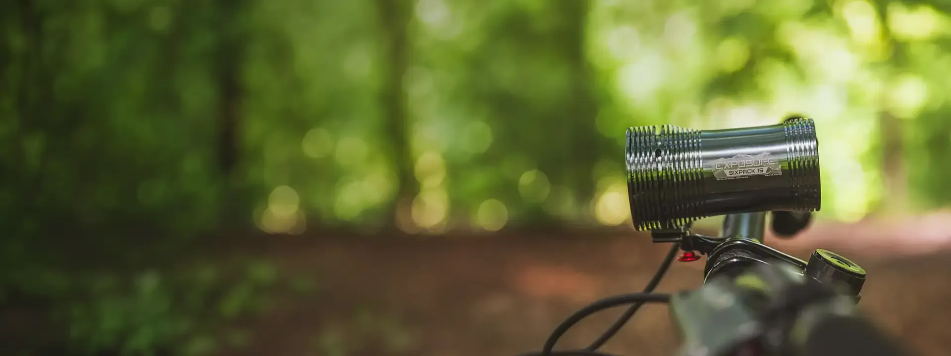 Exposure front bike light mounted on a handlebar beside a woodland trail