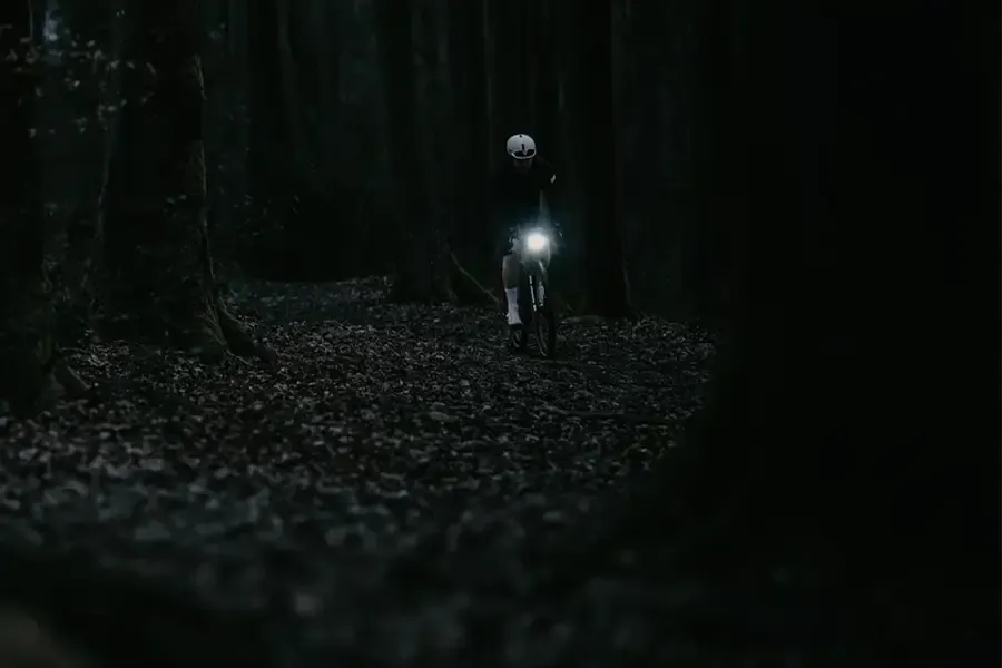 Gravel rider using a front light on a dark forest track