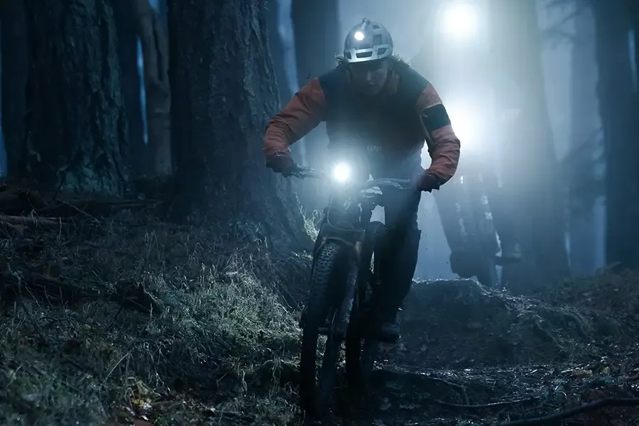 Mountain biker using handlebar and helmet lights on a dark trail