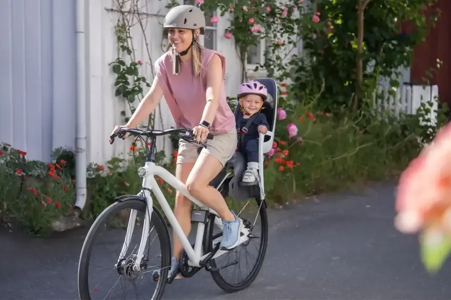 Parent cycling with a helmeted child in a frame-mounted rear bike seat.