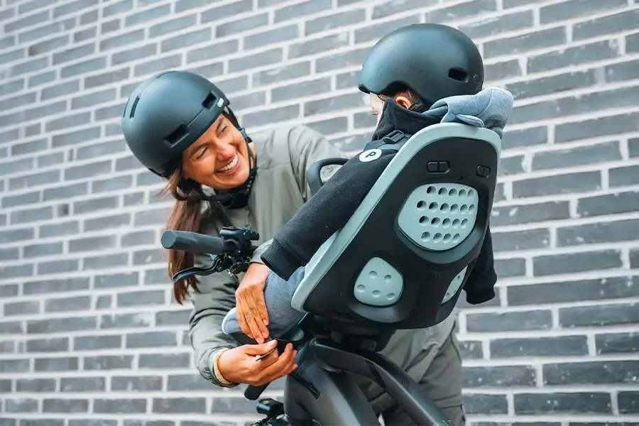 Parent securing a helmeted child in a front-mounted child bike seat.