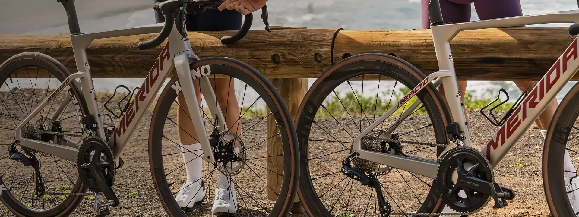 Two road bikes with bottle cages fitted inside their frames beside a wooden fence.