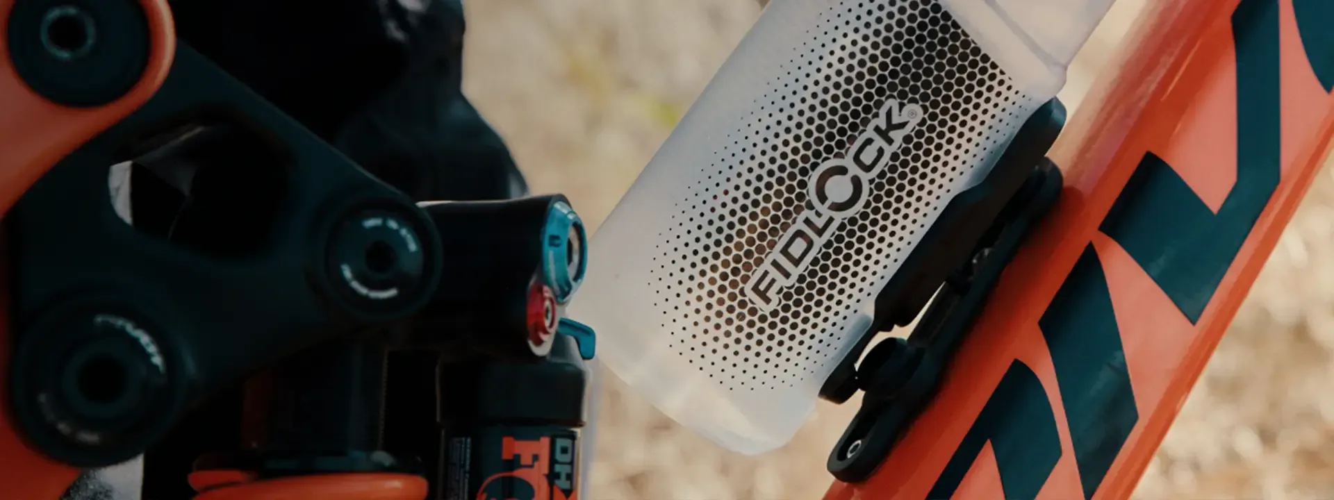 Close-up of a Fidlock water bottle and mounting base on an orange mountain bike frame.