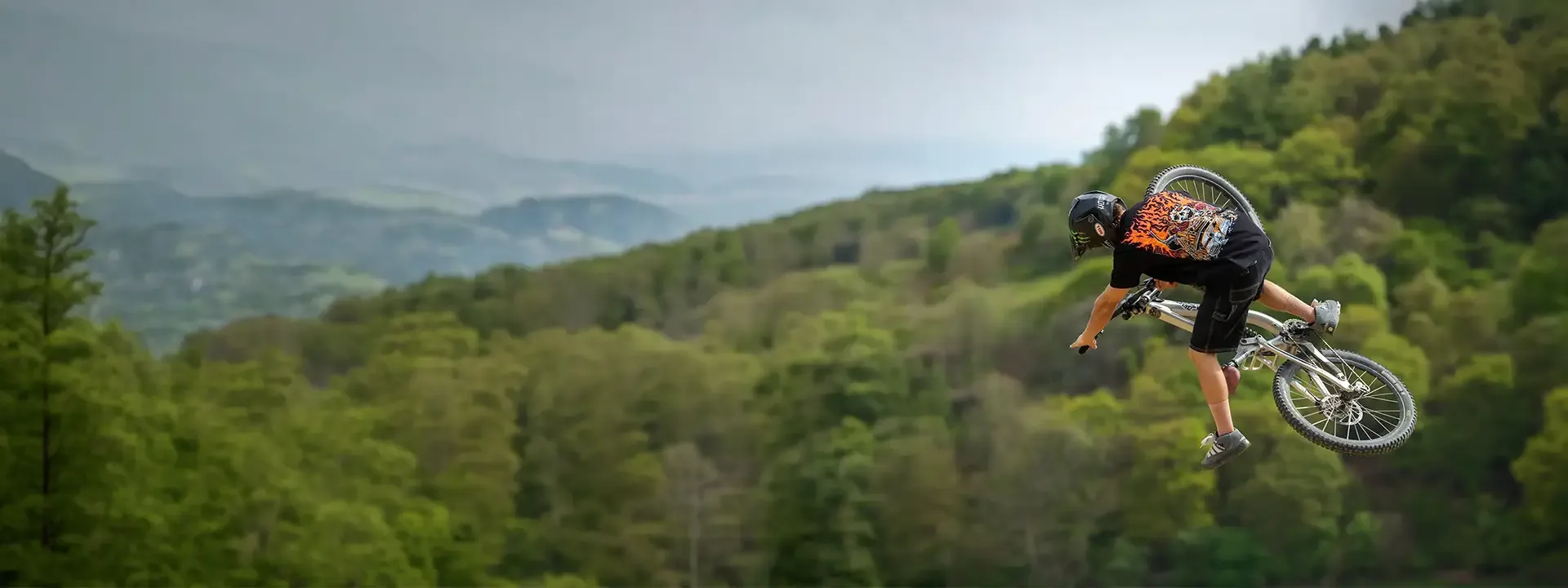 Mountain biker performing an aerial trick above a woodland trail