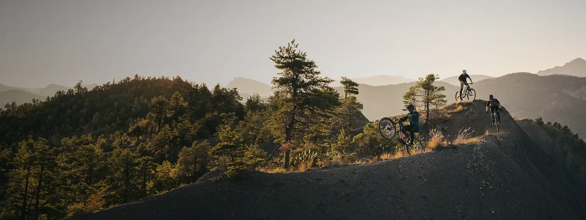 Mountain bikers riding and jumping along an exposed ridge at sunset