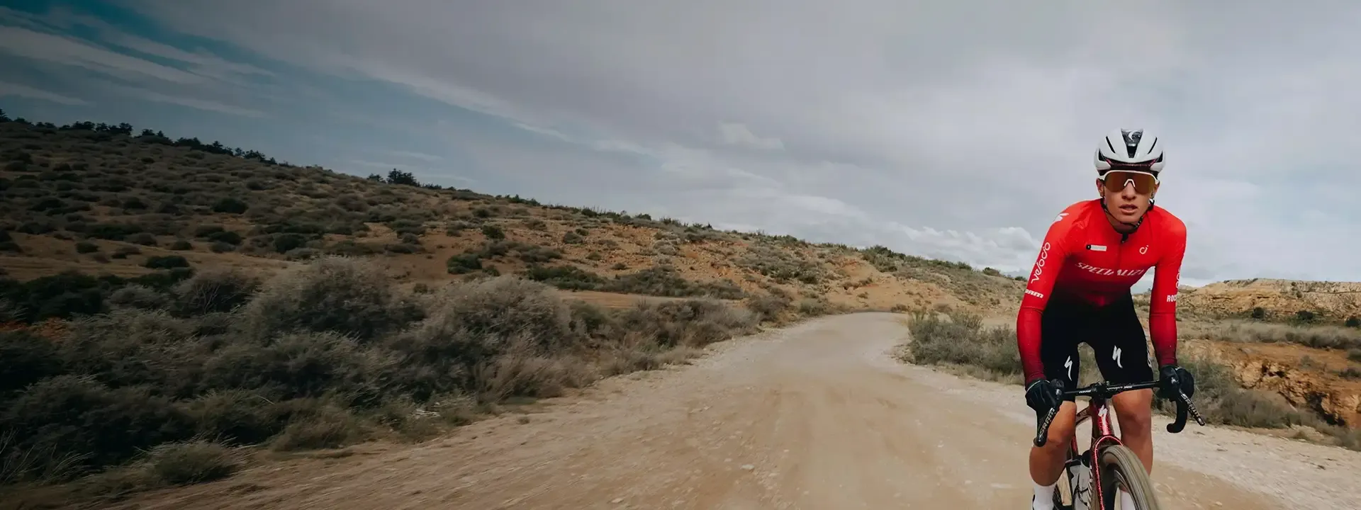 Cyclist wearing a red jersey while riding along an open gravel road through scrubland