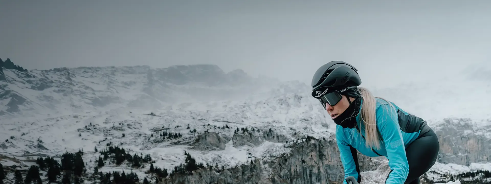 Cyclist riding in snowy winter mountain conditions wearing thermal cycling head warmer beneath a helmet