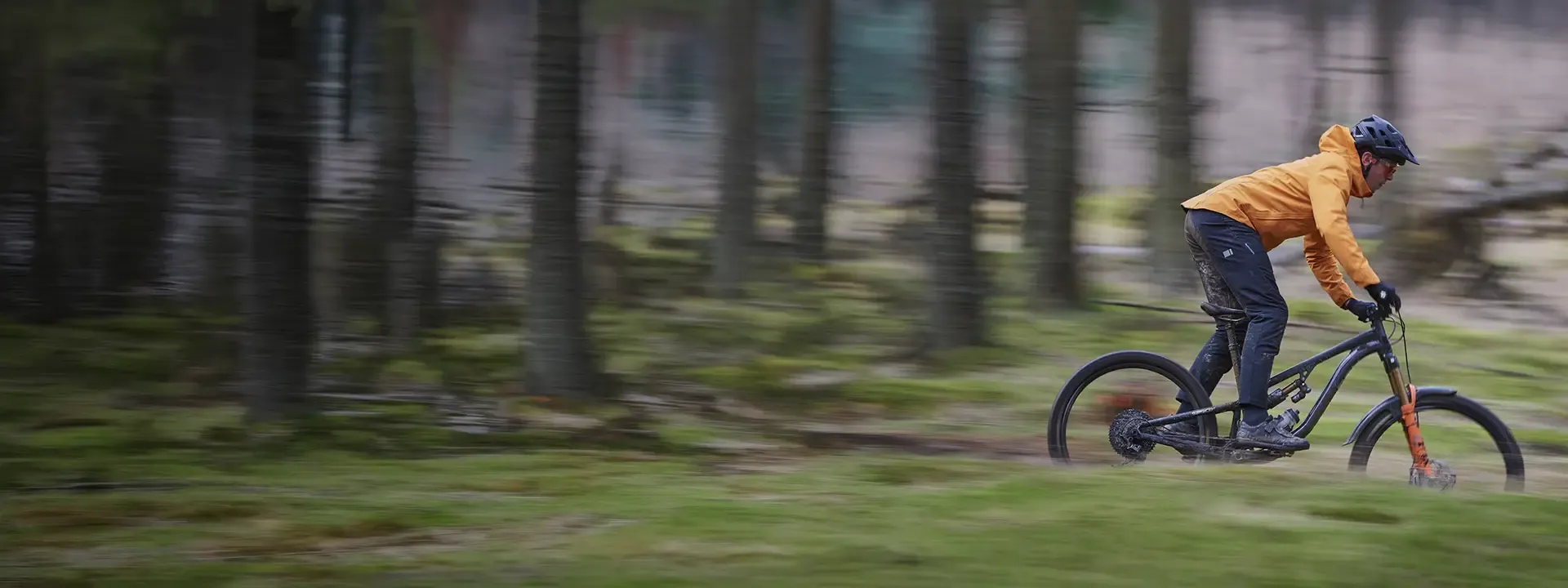 Mountain biker riding through wet forest trails wearing waterproof mountain bike trousers and jacket