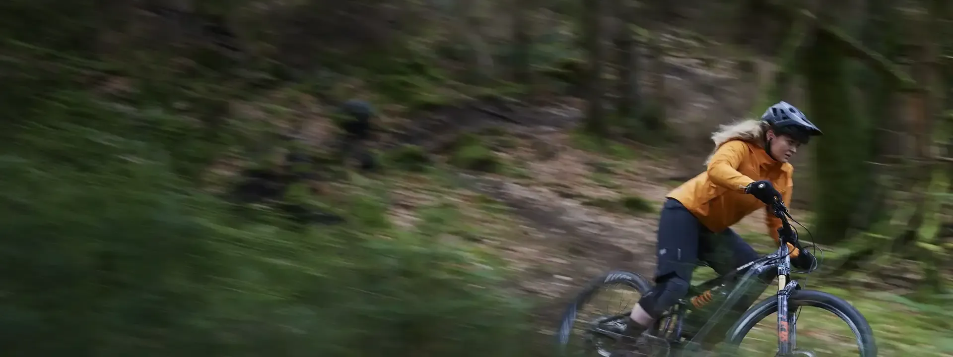 Woman mountain biker riding through woodland wearing a weatherproof cycling jacket