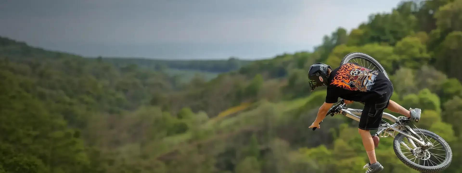 Mountain biker performing a jump while wearing a technical cycling t-shirt on a trail ride