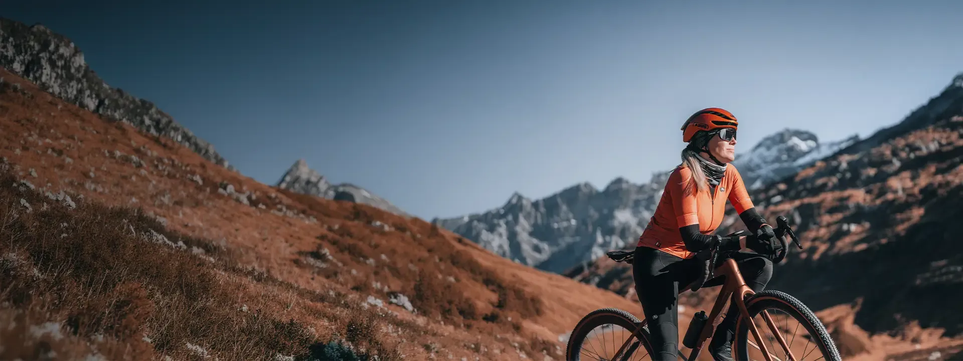 Gravel cyclist riding through mountain terrain wearing arm and leg warmers in cool weather conditions