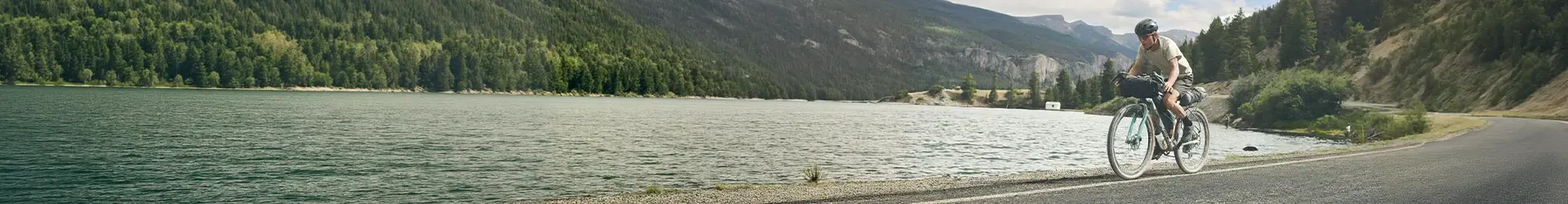Riding a loaded gravel bike past a lake on a bikepacking adventure