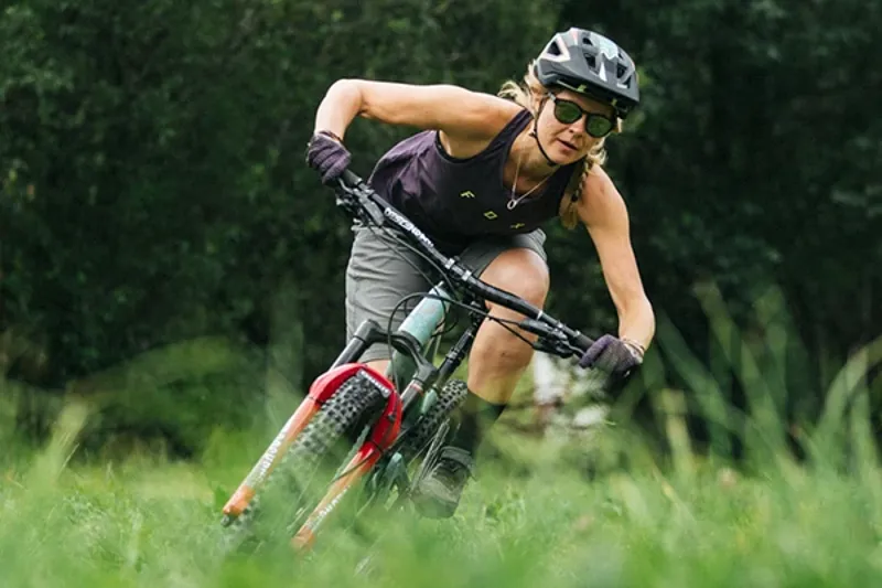 Cyclist wearing women&rsquo;s cycling gloves riding a mountain bike on a flowing trail in the summer