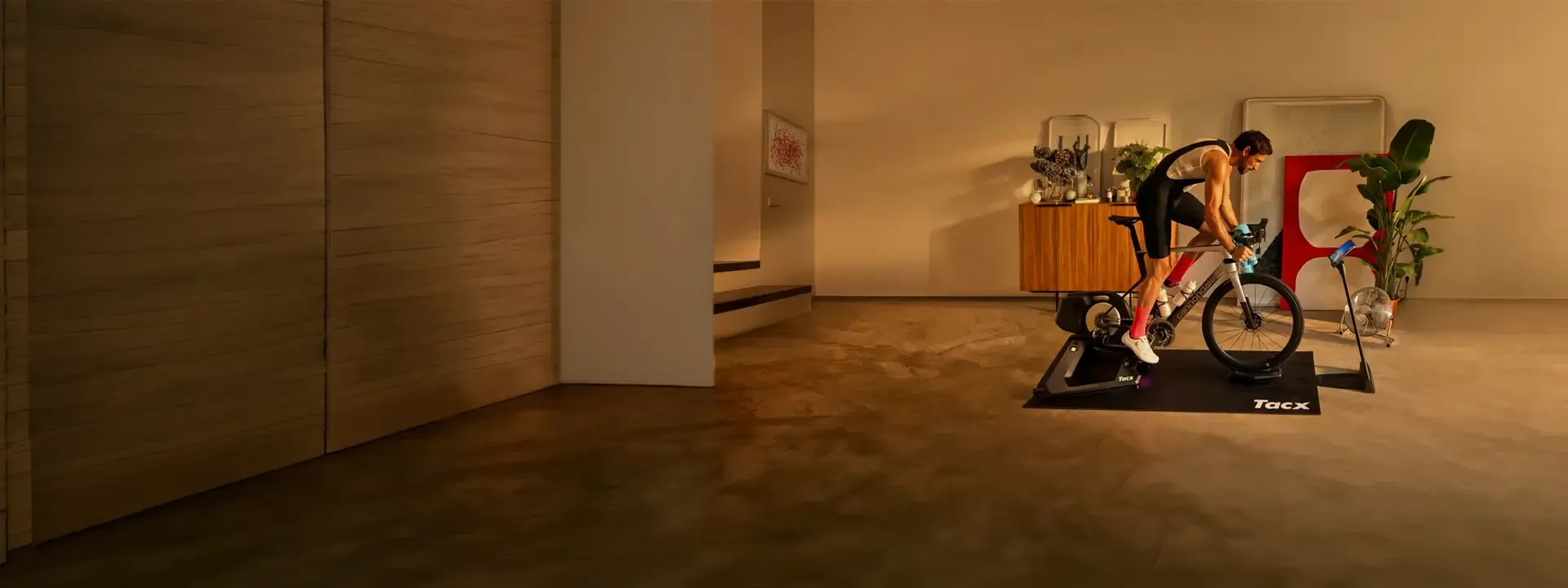 Cyclist riding indoors on a Tacx trainer in a warmly lit room