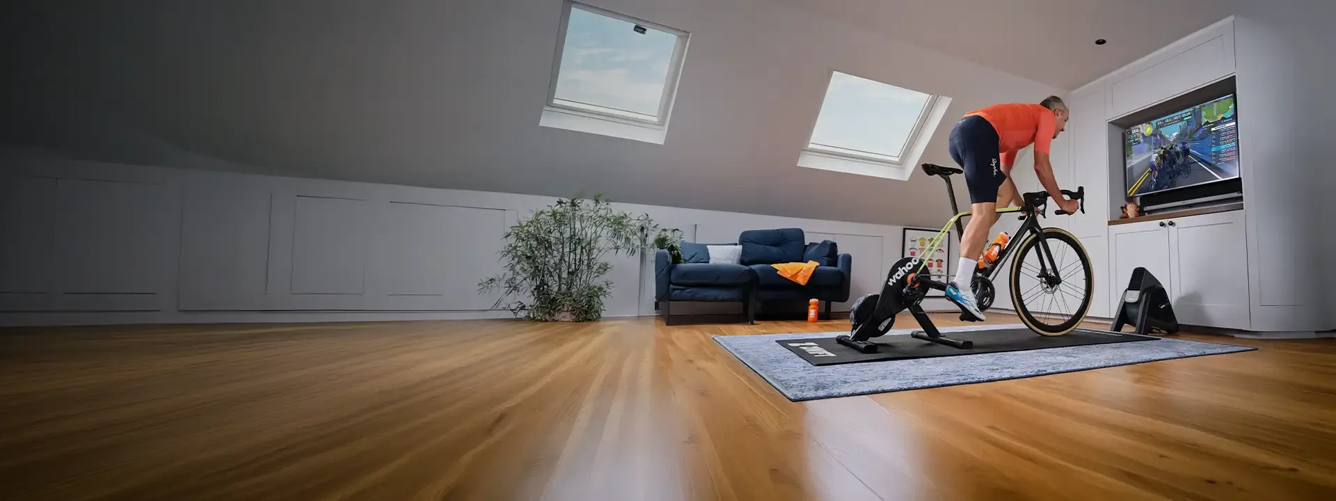 Cyclist training indoors with a floor mat, cooling fan and wall-mounted screen
