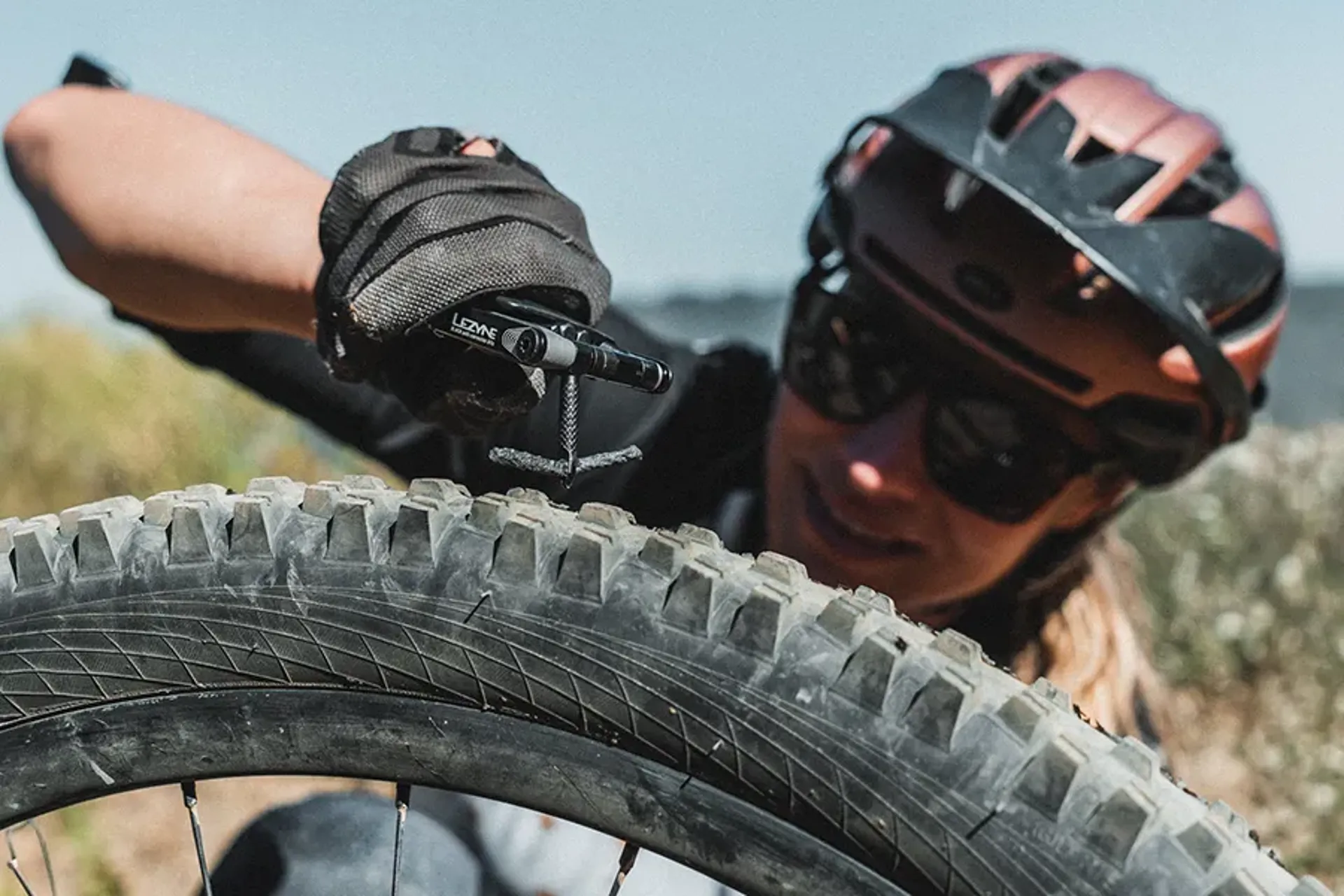A rider using a tubeless plug tool to repair a mountain bike tyre outdoors