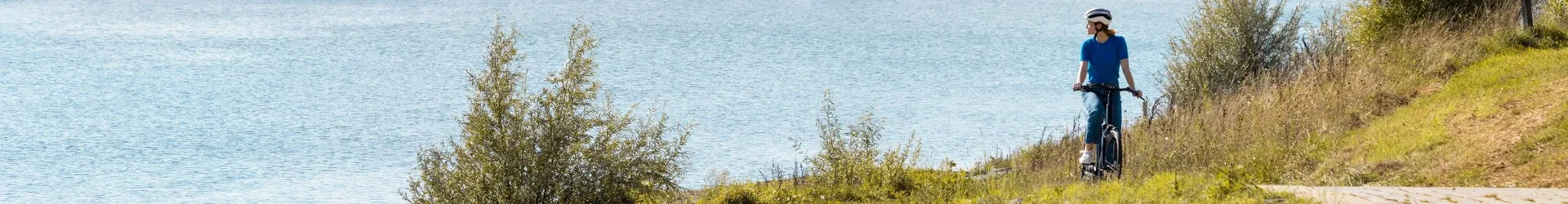 Woman riding a hybrid bike on a path next to a wide waterway