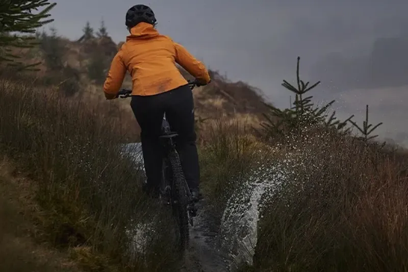 Female mountain biker riding through a puddle wearing waterproof jacket & trousers