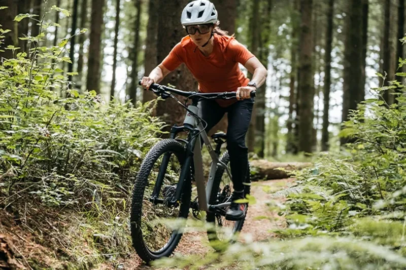 Woman riding a Merida hardtail mountain bike on singletrack in the woods on a sunny day