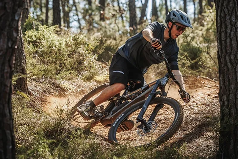 Riding a Merida One-Twenty trail bike on dusty singletrack in the woods on a sunny day
