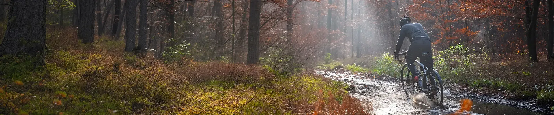 Mountain biker riding through a puddle on a muddy woodland trail