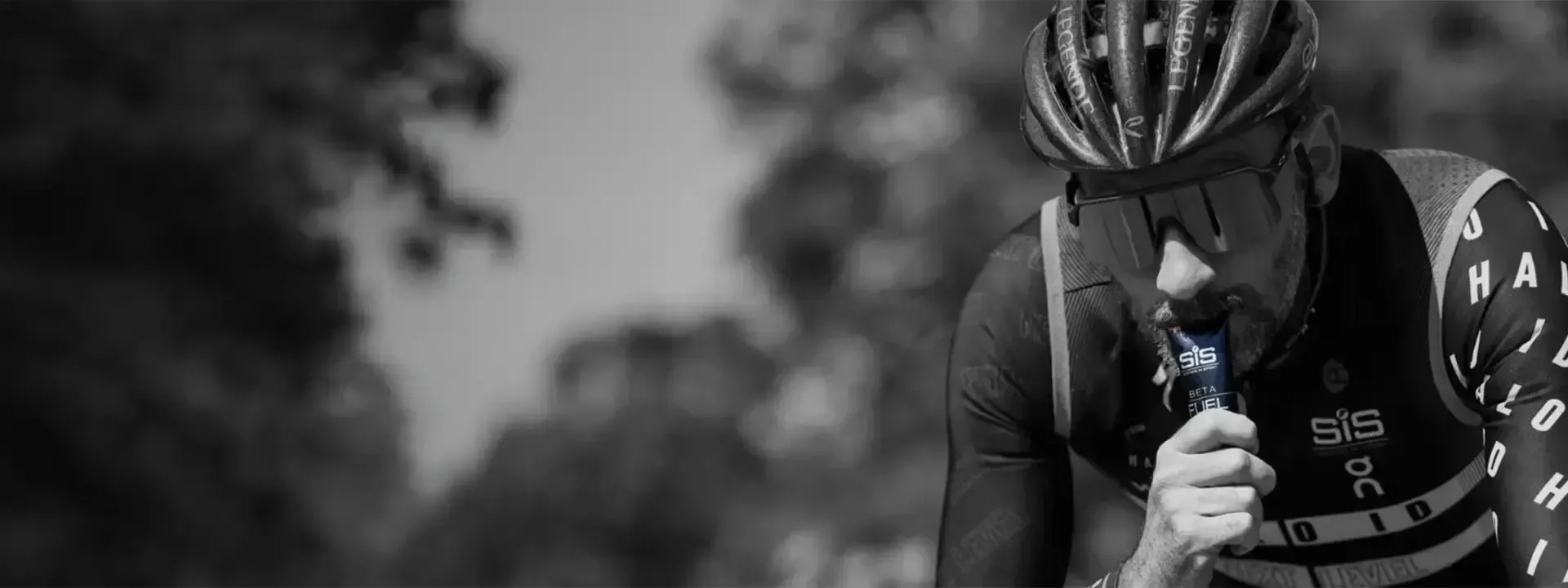 Black-and-white photograph of a helmeted cyclist using a nutrition sachet.