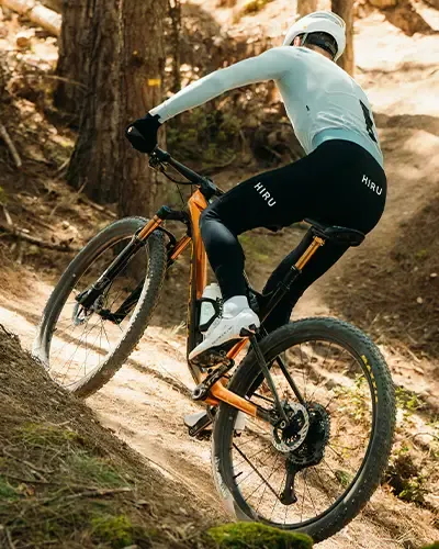 Rider climbing a steep wooded trail on an orange Orbea Oiz