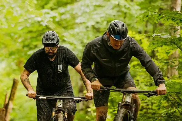 Two riders pedalling Orbea Oiz bikes through woodland