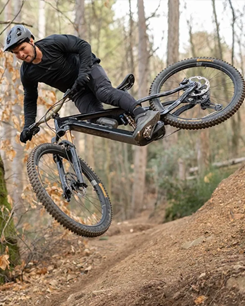 Rider cornering and jumping the Pivot Shuttle AMP&rsquo;d on a forest trail, demonstrating stability and control at speed.