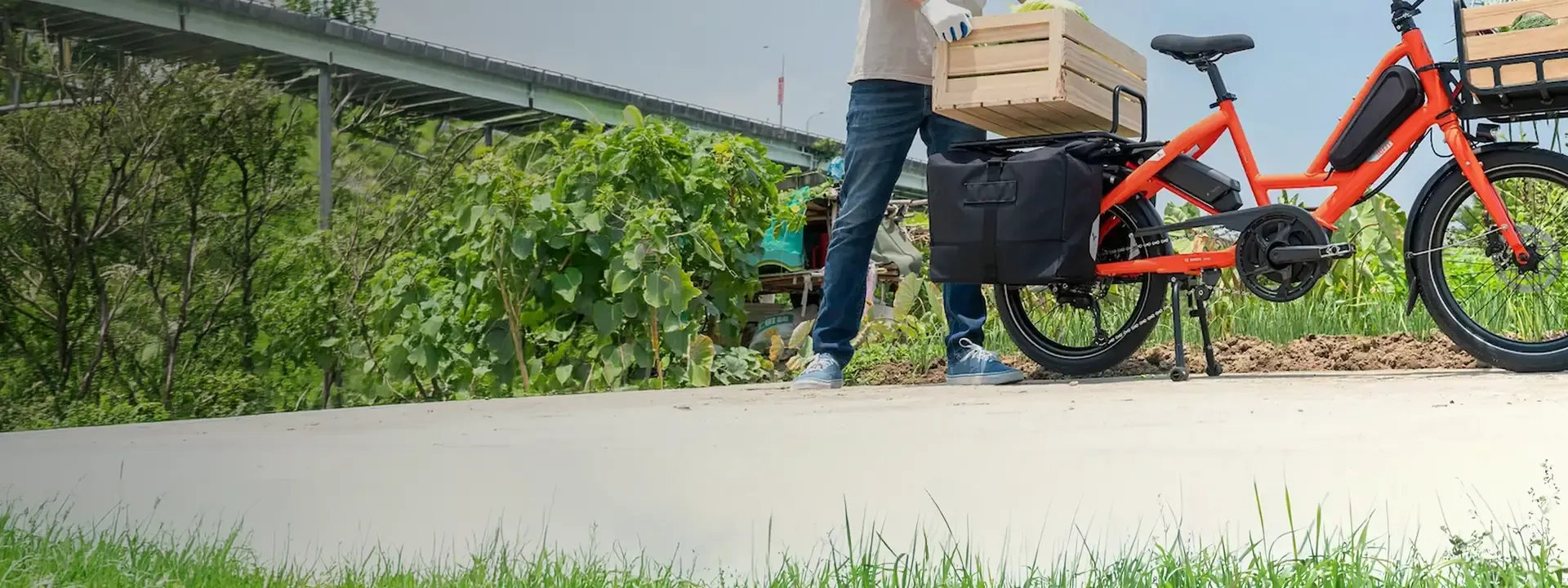 Orange cargo bike parked beside a rider, with luggage fitted.