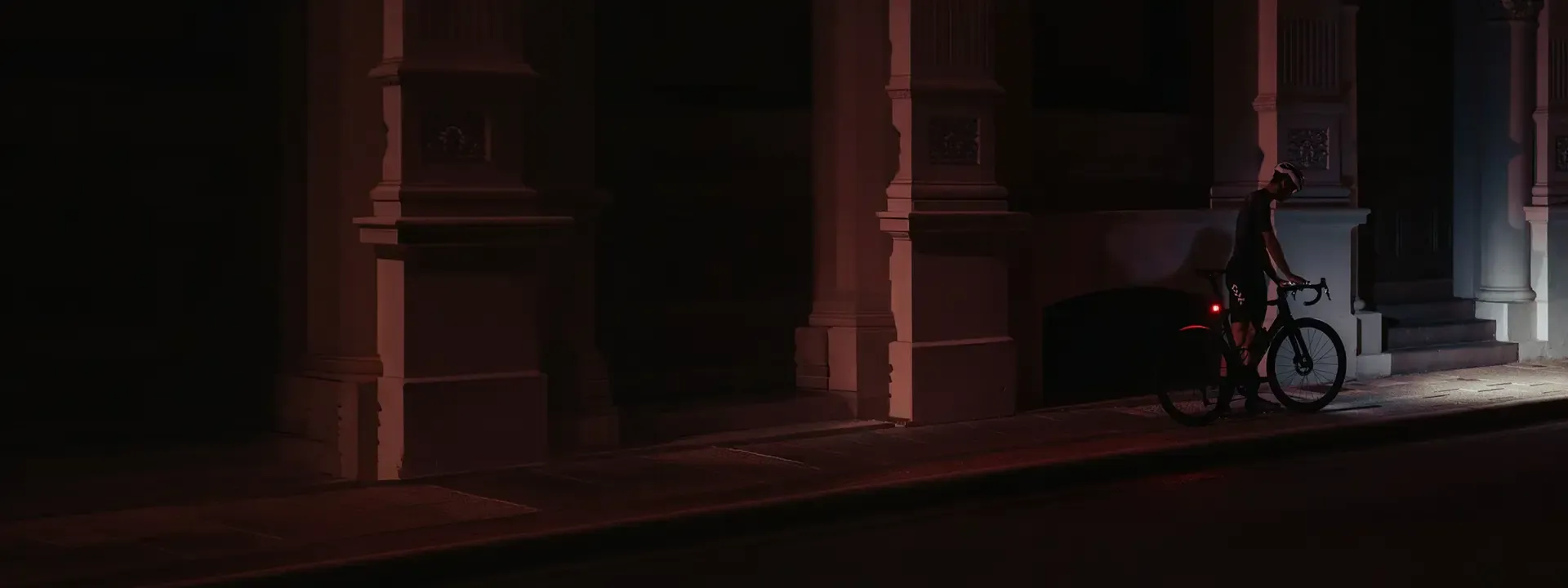 Cyclist riding past a building at night with bike lights illuminated