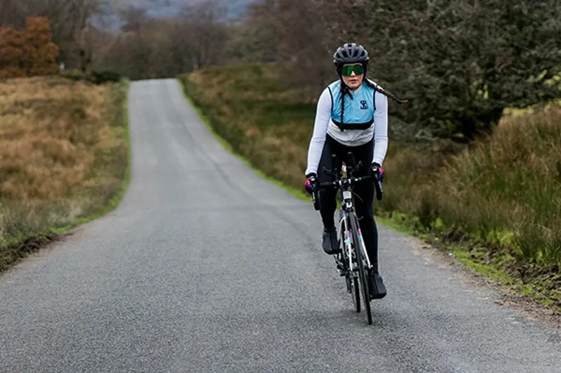 Female road bike rider cycling up a hill on open road in the Welsh hills