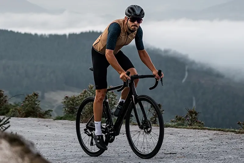 Road cyclist climbing on a misty day wearing a gilet over a short sleeve jersey