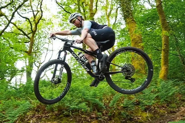 Rider getting steezy on the Specialized Epic 9 XC race bike in action on a woodland jump