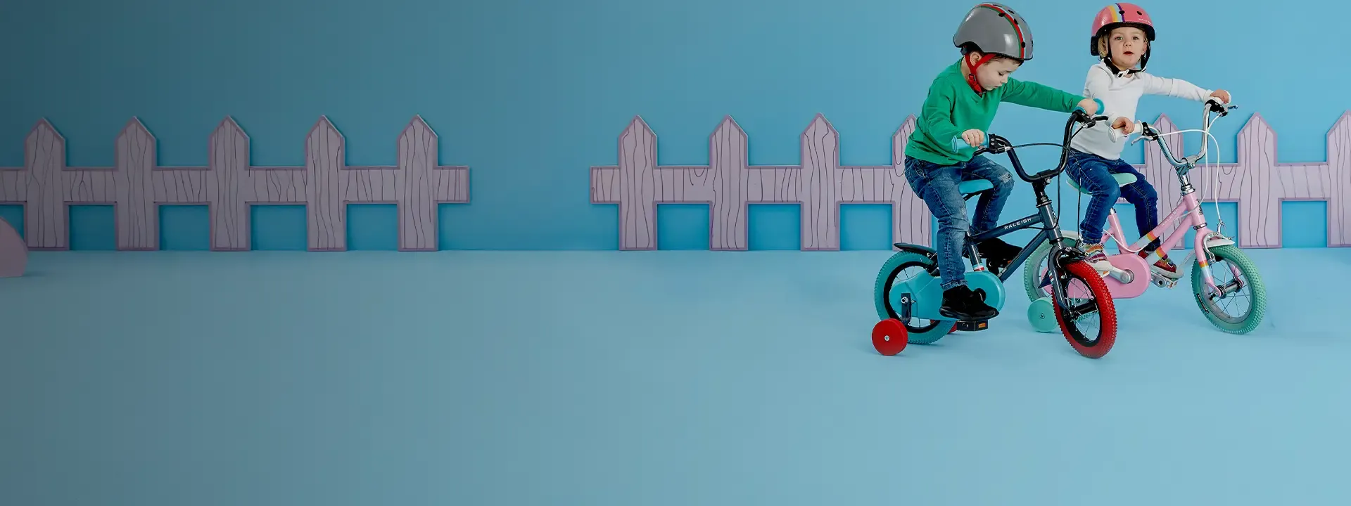 Two children wearing helmets riding small bikes with stabilisers.