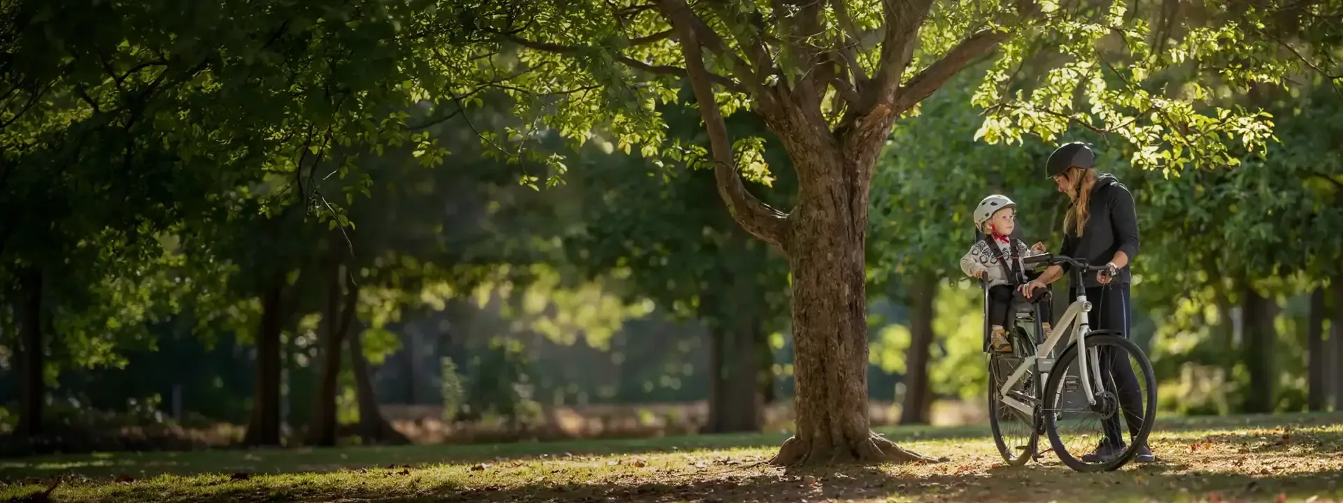 Parent cycling through a leafy park with a child in a rear bike seat
