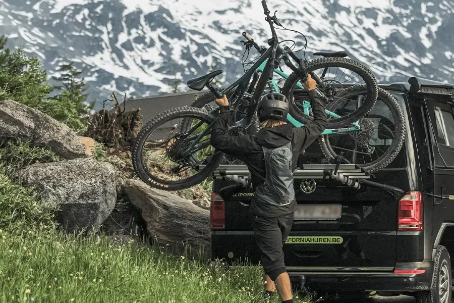 Man placing a mountain bike onto a car rack on a camper van