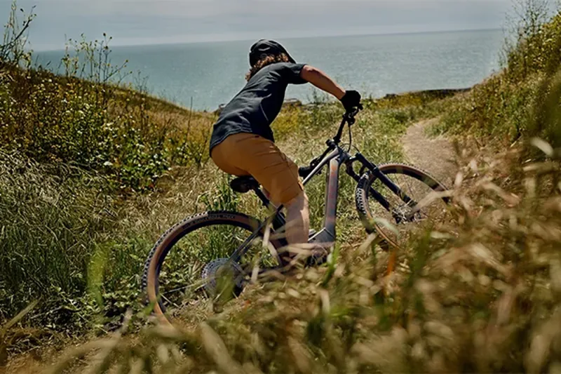 Riding the Trek Marlin+ hardtail eMTB on a singletrack trail by the coast