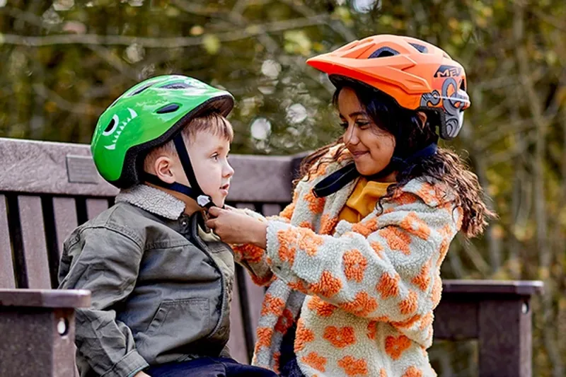 two children helping each other to put on bicycle helmets