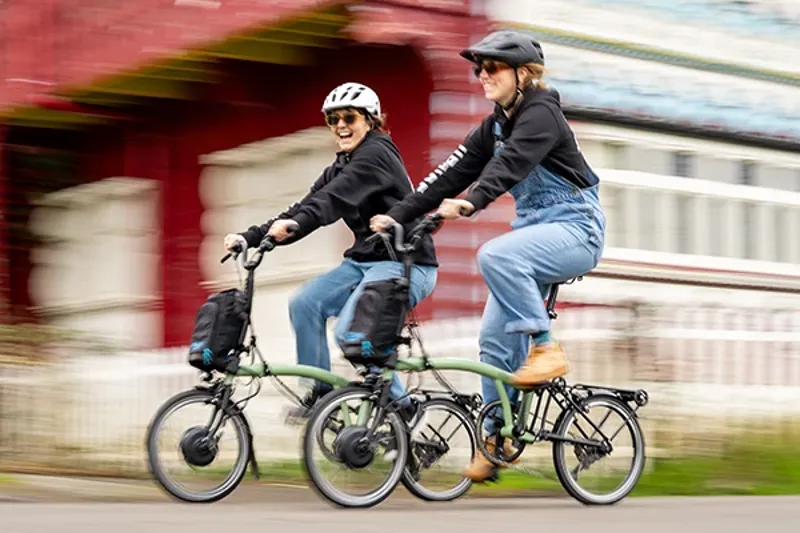 rtwo women riding brompton electric bikes with Urban commuter helmets in the park